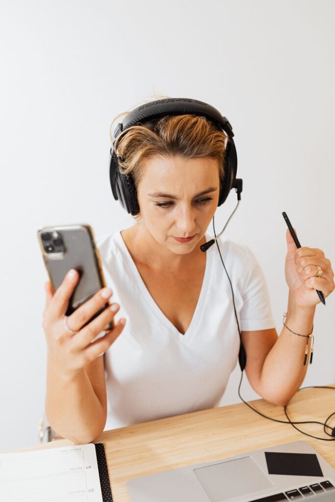 Woman in a headset concentrating on work with smartphone and laptop. Ideal for business tech imagery.
