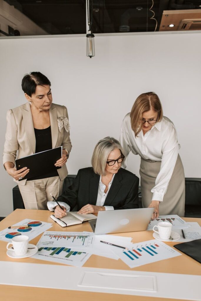 pexels-photo-7433868-7433868 Three professional women working together on a business project with charts and laptops in a modern office.